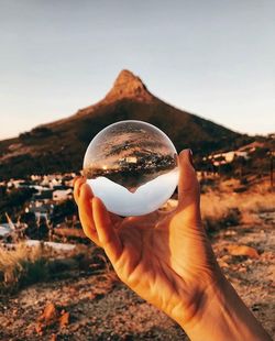 Midsection of person holding crystal ball against sky