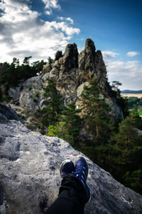 Low section of person on rock in mountains against sky