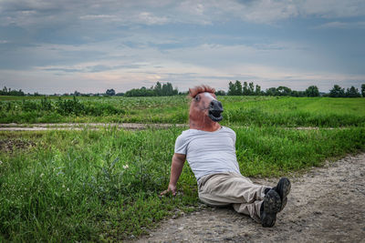Mid adult man wearing mask sitting on land against sky