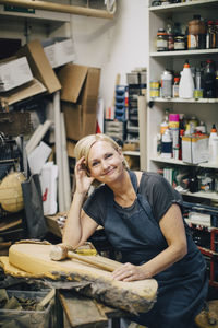 Portrait of confident female upholstery worker sitting at workbench in workshop