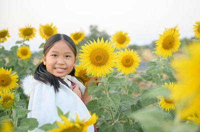 Portrait of smiling girl amidst sunflower field against sky