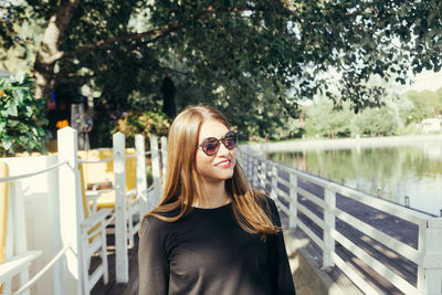 Portrait of smiling young woman by railing against trees