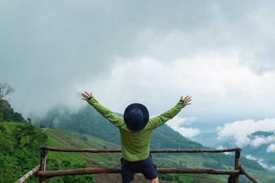 Rear view of man with arms raised on landscape against sky