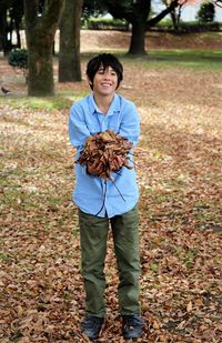 Smiling boy holding dry leaves while standing on field