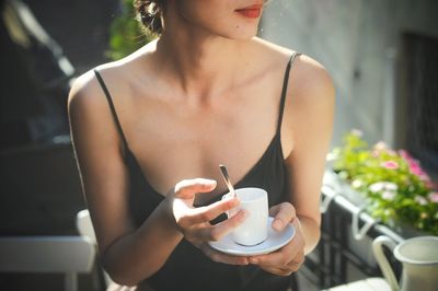 Midsection of woman holding coffee while sitting outdoors