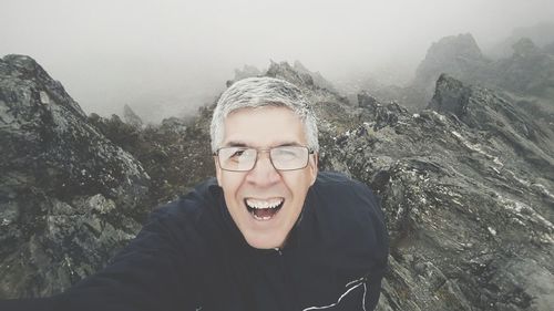 Portrait of smiling man standing on rock against sky