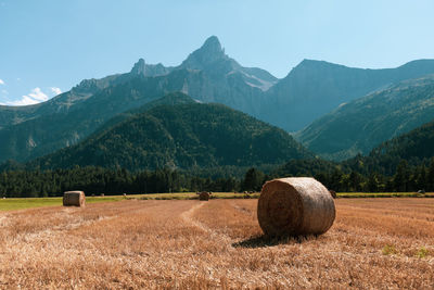 Hay bales on field by mountains against sky