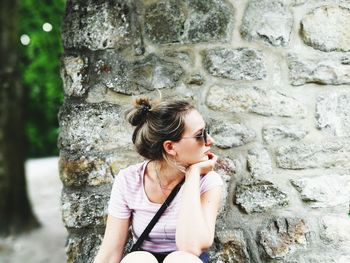 Woman looking away while standing against brick wall