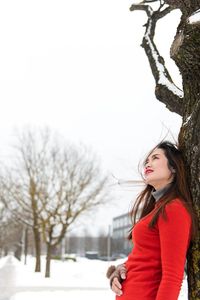 Woman leaning on tree against sky during winter