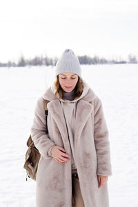 Young girl in beige clothes, fur coat made of artificial fur walks in winter