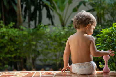 A charming toddler sits on the steps of a house in the sunlight. back view.