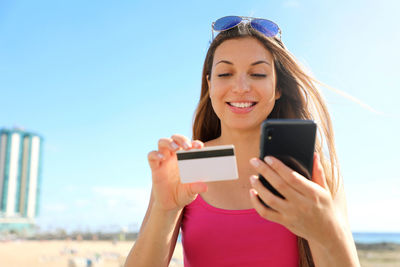 Close-up of cute young woman reading credit card number for payment online outdoor on summer.