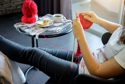 Midsection of woman knitting wool while sitting at home