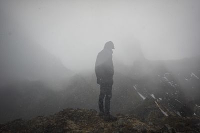 Man standing on rock against sky during winter