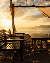 Chairs and table at beach against sky during sunset