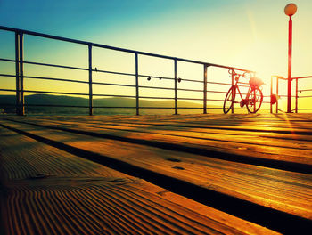 Bicycle parked by railing against sky during sunset