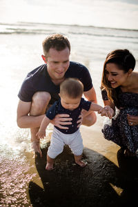 Mid 30's parents playing in ocean with infant son