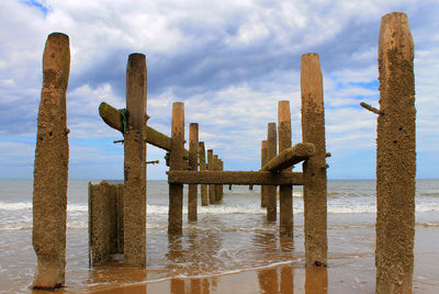 Wooden posts on beach against sky