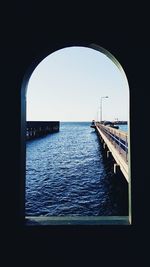 Sea against clear sky seen through arch window