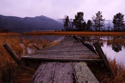 Wooden bench on field by lake against sky