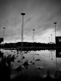 Reflection of silhouette street lights in lake against sky