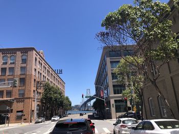 Cars on street by buildings against clear blue sky