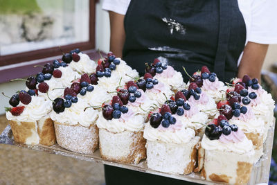 Female baker holding tray of pastries outside cafe