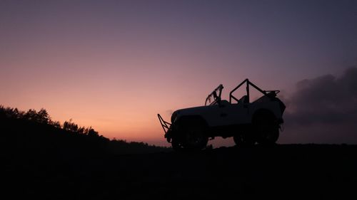 Silhouette vehicle on field against sky during sunset
