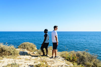 Rear view of friends standing on beach against clear blue sky