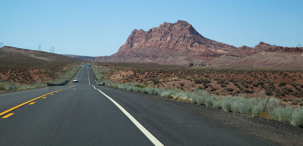 Road leading towards mountains against clear sky