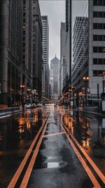 Illuminated road amidst buildings in city during rainy season