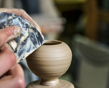 Potter makes a pretty small vase from clay, using the tool for surface leveling close-up 