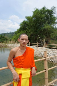 Portrait of monk standing by railing against trees and sky