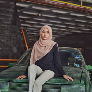 Thoughtful beautiful young woman in hijab sitting on old car