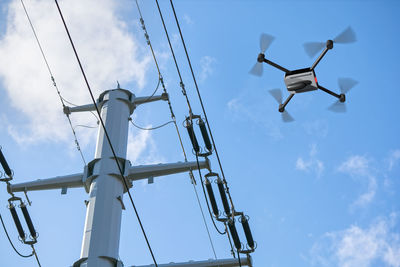 Low angle view of drone flying by electricity pylon against sky