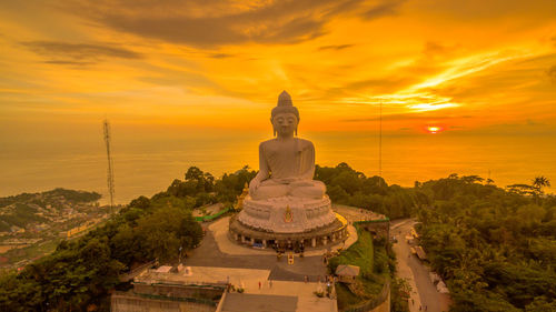 Statue amidst buildings against sky during sunset