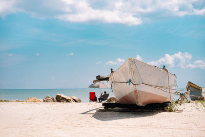 Moored boat and man on beach chair on beach against sky in summer