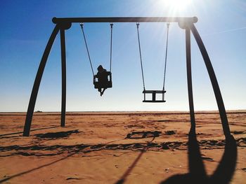 Boy playing swing on sand against clear sky