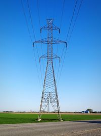 Low angle view of electricity pylon on field against clear blue sky