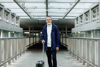 Portrait of man with luggage standing on footpath at airport