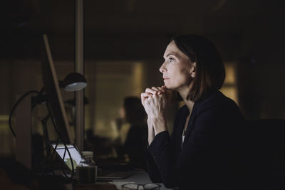 Mature businesswoman with hands clasped working over computer in office at night