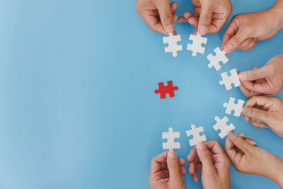 Cropped hands of person holding jigsaw piece against blue background