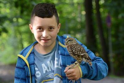Portrait of boy holding owl against trees