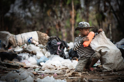 Cute boy sitting by garbage outdoors