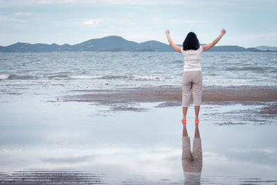 Rear view of woman standing at beach against sky