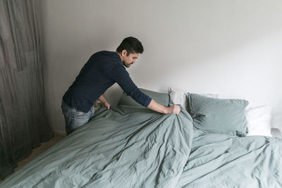 High angle view of man making bed while standing in bedroom at home