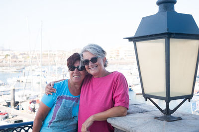 Portrait of smiling friends standing by railing at harbor
