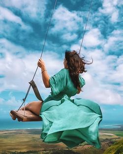 Woman sitting on swing at shore against sky