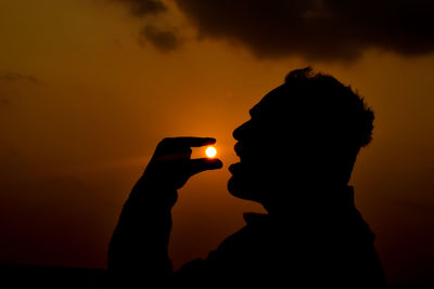 Optical illusion of silhouette man eating sun during sunset