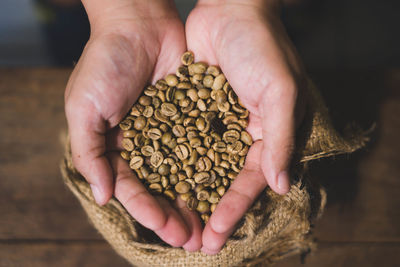 High angle view of person hands holding raw coffee beans